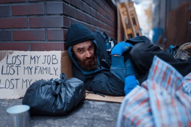 Bearded beggar sleeping on city street. Poverty is a social problem, homelessness and loneliness, alcoholism and drunk addiction