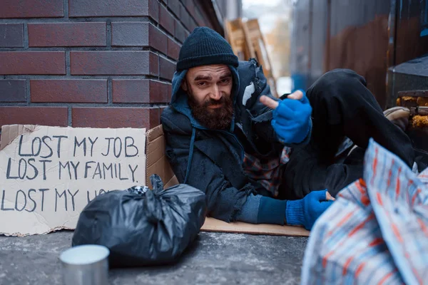 Bearded beggar sleeping on city street. Poverty is a social problem, homelessness and loneliness, alcoholism and drunk addiction