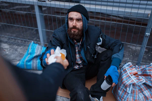 男は都会の通りで髭を生やした汚い乞食に食べ物を与える 貧困は社会問題 ホームレスや孤独 アルコール依存症や飲酒依存症 都市部の孤独 — ストック写真