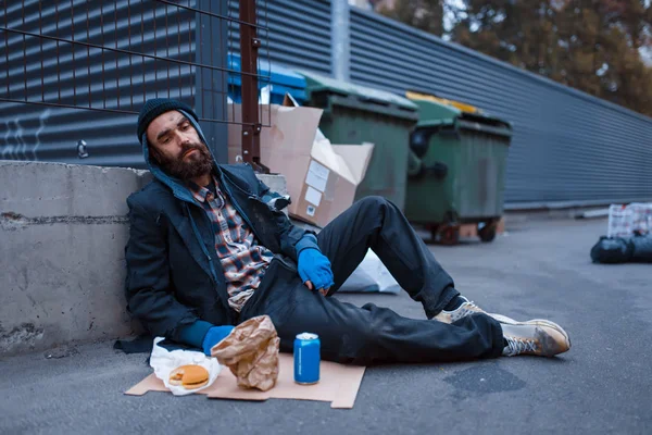 髭を生やした汚れた乞食の食べ物が街の通りにあるゴミ箱に座っている 貧困は社会問題 ホームレスや孤独 アルコール依存症や飲酒依存症 都市部の孤独 — ストック写真