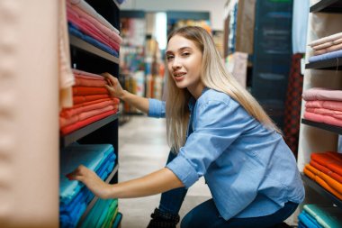 Tezgahtar kadın tekstil dükkanında kumaş ölçer. Arka planda dikiş dikmek için kumaşlı raflar, mağazada kıyafet seçimleri