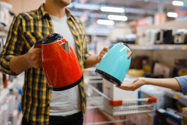 Young couple choosing electric kettle in electronics store. Man and woman buying home electrical appliances in market clipart