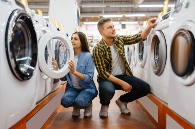 Elektronik mağazasından çamaşır makinesini seçen aile çifti. Erkek ve kadın marketten ev aletleri satın alıyorlar.