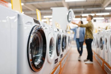 Elektronik mağazasından çamaşır makinesini seçen aile çifti. Erkek ve kadın marketten ev aletleri satın alıyorlar.