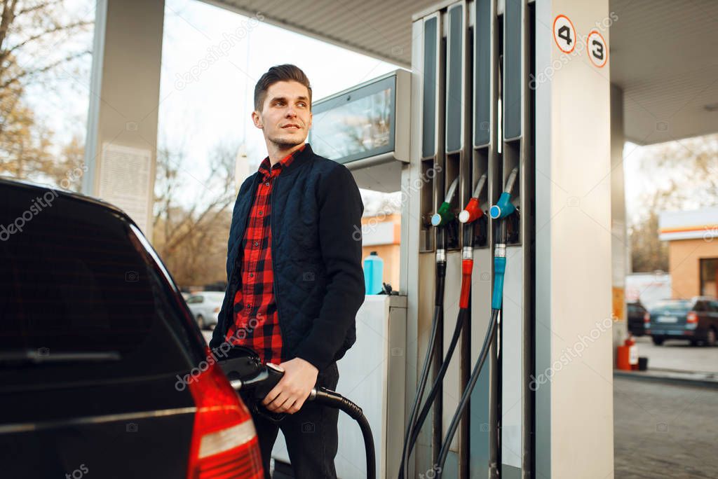 Man with gun fuels vehicle on gas station, bottom view, fuel filling. Petrol fueling, gasoline or diesel refuel service