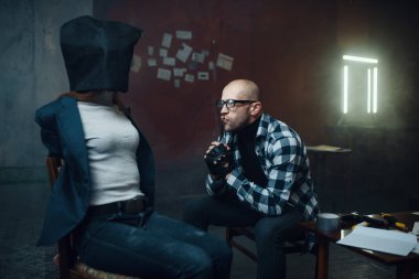 Maniac kidnapper looks on his female victim with a bag on her head. Kidnapping is a serious crime, crazy male psycho, kidnap horror, violence