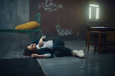 Manyak fidyecinin kadın kurbanı yatağa kelepçeli bir şekilde yerde uyuyor. Adam kaçırma ciddi bir suçtur. Dehşet, şiddet.