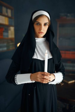Cüppeli genç rahibe elinde mum tutuyor. Rahibe manastırda ibadet için hazırlanıyor, din ve inanç, dindar insanlar.
