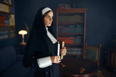 Cüppeli genç rahibe elinde bir kitap ve mum tutuyor. Rahibe manastırda ibadet için hazırlanıyor, din ve inanç, dindar insanlar.