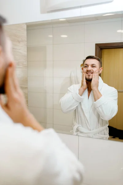 バスローブの男は バスルーム ルーチン式の朝の衛生で鏡の上に顔を剃った シンクの男性は 皮膚や体の治療手順を実行します — ストック写真