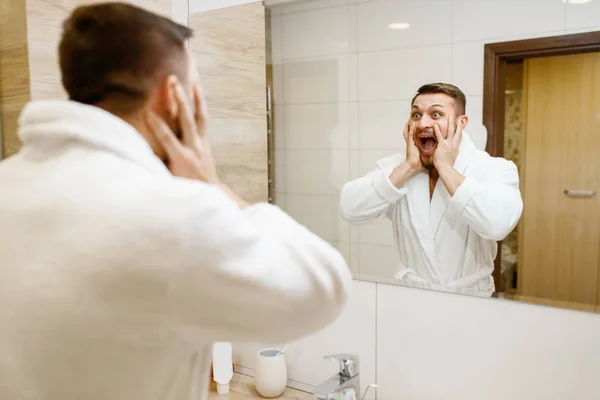 ひげを生やした男は バスルームの鏡で 朝の衛生状態で彼の外観におびえた シンクの男性は 皮膚や体の治療手順を実行します — ストック写真