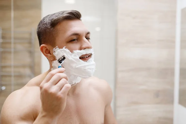 男人在浴室里用剃须刀刮胡子 这是每天早上的卫生习惯 水槽处的男性进行皮肤和身体治疗 — 图库照片