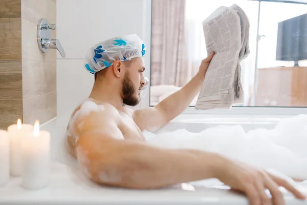 男は新聞を泡で読み取り 朝の衛生状態 男性はバスルーム 皮膚やボディトリートメントの手順でリラックス — ストック写真