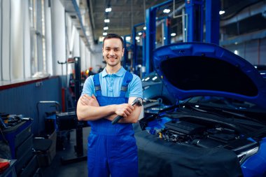 Üniformalı işçi asansördeki araçta duruyor, servis istasyonunda. Otomobil denetimi ve denetimi, profesyonel teşhis ve onarım