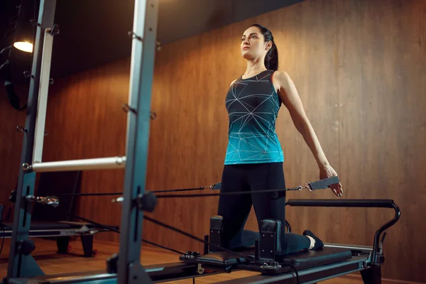 Spor giyimli zayıf bir kadın, spor salonunda egzersiz makinesinde pilates eğitimi alıyor. Spor kulübünde spor eğitimi. Atletik kadın, aerobik.