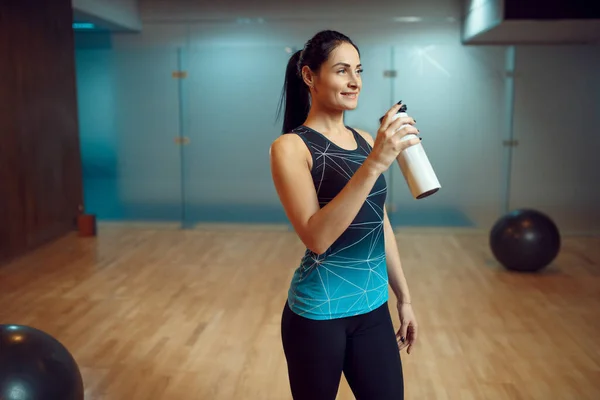 Smiling woman drinks water after pilates training in gym, healthy lifestyle. Fitness workuot in sport club. Athletic female person, aerobics indoor, body stretching