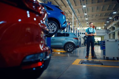 Tamirci asansörlerdeki araçlarda duruyor, araba servis istasyonunda. Otomobil denetimi ve denetimi, profesyonel teşhis ve onarım
