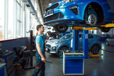 Üniformalı işçiler aracın altını kontrol ediyor. Asansörde, servis istasyonunda. Otomobil denetimi ve denetimi, profesyonel teşhis ve onarım