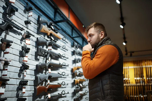 銃屋のショーケースで拳銃を見てる男 武器店に立つハンターのための機器 狩猟やスポーツシューティング趣味 — ストック写真