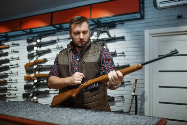 銃屋のカウンターにライフルを持った男 武器店に立つハンターのための機器 狩猟やスポーツシューティング趣味 — ストック写真