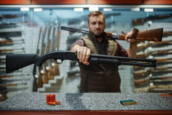 銃屋のカウンターにライフルを２丁持った男 武器店に立つハンターのための機器 狩猟やスポーツシューティング趣味 — ストック写真