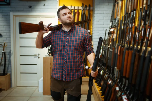 銃屋のショーケースで男は2本のライフルでポーズ 武器店に立つハンターのための機器 狩猟やスポーツシューティング趣味 — ストック写真