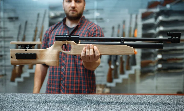 Male person shows pneumatic rifle at showcase in gun shop. Euqipment for hunters on stand in weapon store, hunting and sport shooting hobby