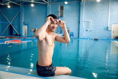 Yüzme gözlüklü erkek yüzücü havuzda poz veriyor. Havuz başındaki adam, su aerobiği hocası suda poz veriyor.