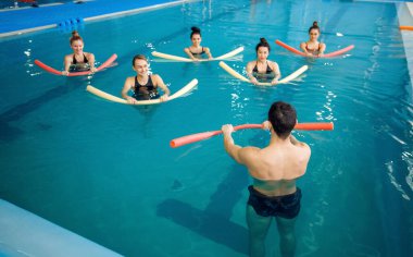 Erkek eğitmen ve kadın grup, havuzda su aerobiği eğitimi. Sudaki erkek ve kadınlar, spor yüzme egzersizleri.