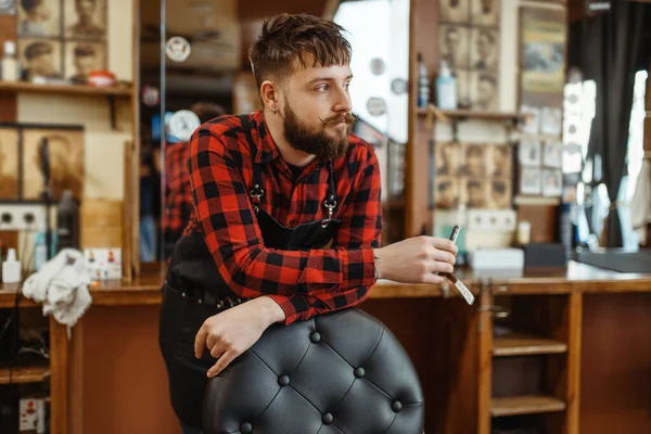 剃须刀刀片理发师摆姿势坐在椅子上 专业理发店是一种时髦的职业 复古风格美发店的男性理发师 裁剪配件 — 图库照片