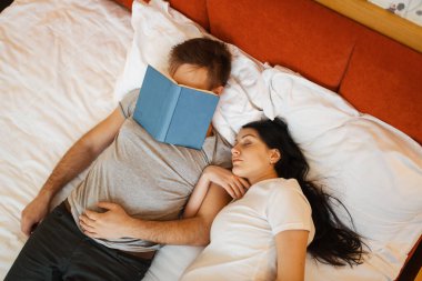 Koca ve göbekli hamile karısı evde, yatak odasında arka planda yatıyorlar. Hamilelik, doğum öncesi dönem. Müstakbel annem ve babam kanepede, sağlık hizmetlerinde dinleniyorlar.