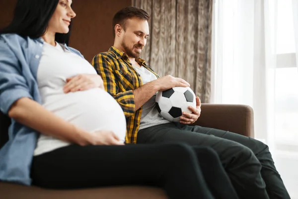 ボールを持つ夫と腹を自宅で冗談で彼の妊娠中の妻 ユーモア 妊娠期間 期待されるお母さんとお父さんはソファで休んでいます 健康管理 — ストック写真