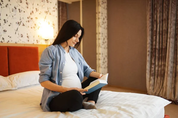 有肚子饿的孕妇在床上看书 产前的平静 准妈妈在卧室休息 — 图库照片