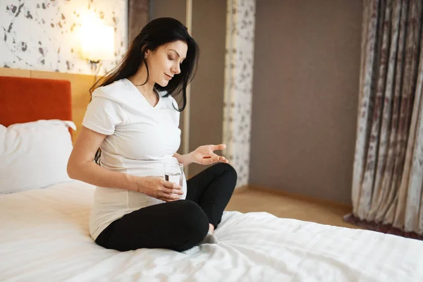 腹を持つ妊婦は自宅で錠剤を服用します 出生前の期間で穏やかな 期待されるお母さんはベッドルームで休み 健康的なライフスタイル — ストック写真