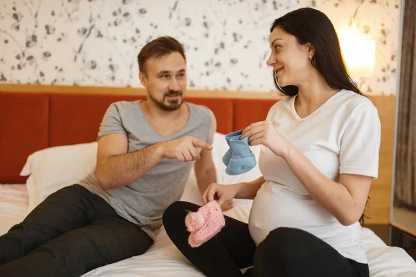 Счастливая Пара Беременная Жена Животом Показывает Мужу Одежду Новорожденных Дома — стоковое фото
