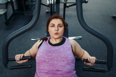 Spor salonunda egzersiz makinesinde şişman bir kadın, üst düzey, aktif eğitim. Kadın aşırı kilolarla, obeziteye karşı aerobik egzersizlerle, spor kulüpleriyle mücadele ediyor.