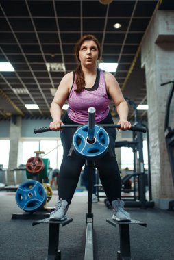 Kilolu bir kadın spor salonunda barla egzersiz yapıyor, aktif antrenman yapıyor. Obez kadın aşırı kilolarla, obeziteye karşı aerobik egzersizlerle, spor kulüpleriyle mücadele eder.