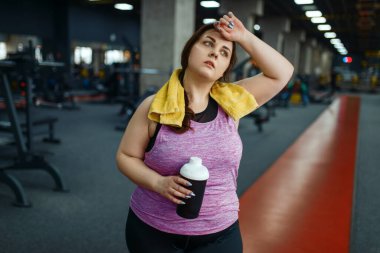 Kilolu kadın spor salonunda diyet kokteyli içiyor, aktif eğitim görüyor. Obez kadın aşırı kilolarla, obeziteye karşı aerobik egzersizlerle, spor kulüpleriyle mücadele eder.