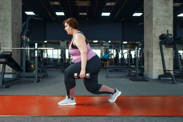 Overweight woman doing exercise with dumbbells in gym, active training. Obese female person struggles with excess weight, aerobic workout against obesity, sport club