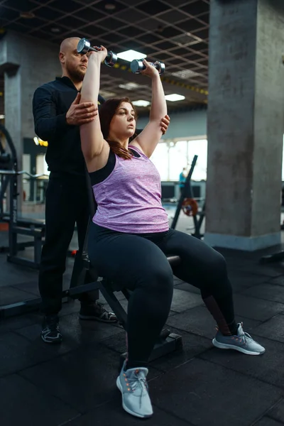 体重增加的女子与教练一起在体育俱乐部做哑铃运动 与教练一起做健身训练 女性与超重 有氧运动 体操等问题作斗争 — 图库照片