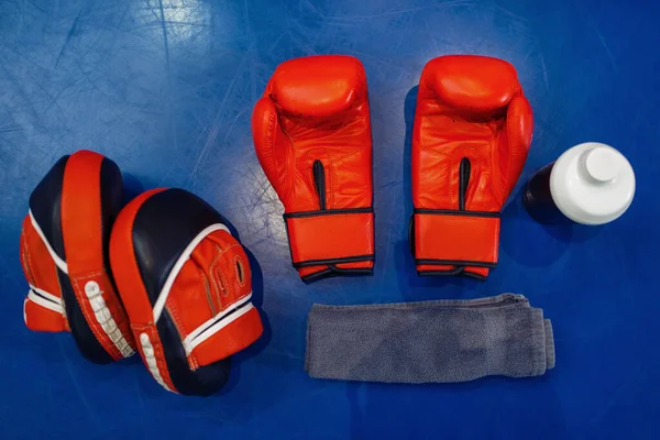 Pair of red boxing gloves, workout pads and equipment on ring canvas, top view, nobody. Box or kickboxing sport concept, training tools, fighting martial arts