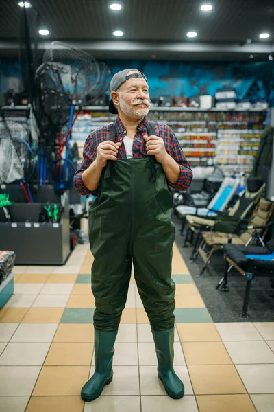Рыбак Примеряет Резиновый Комбинезон Рыболовецком Магазине Крючки Безделушки Заднем Плане — стоковое фото