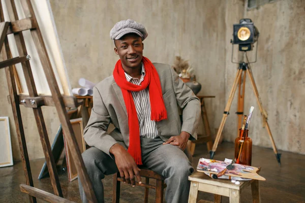 穿着帽子和红围巾的时髦男画家在艺术工作室的画架前摆姿势 画家在他的工作场所画画 在车间里创作大师作品 — 图库照片