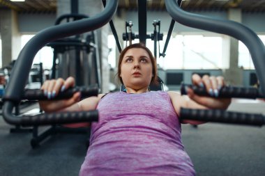 Spor salonunda egzersiz makinesinde şişman bir kadın, üst düzey, aktif eğitim. Kadın aşırı kilolarla, obeziteye karşı aerobik egzersizlerle, spor kulüpleriyle mücadele ediyor.