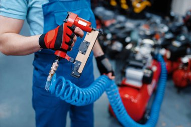 Üniformalı erkek işçi alet deposunda pnömatik çivi tutuyor. Hırdavatçıda profesyonel ekipman seçimi, enstrüman süpermarketi