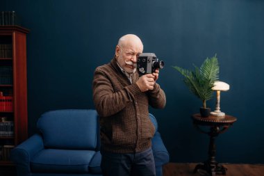 Yaşlı adam eski bir kamerayla merkez büroda poz veriyor. Oturma odasında yaşlı sakallı, yaşlı bir işadamı.
