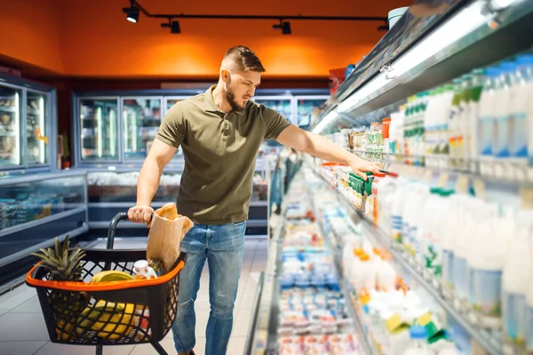 食料品店 乳製品部門でヨーグルトを選択する男 スーパーマーケットでカートで飲料や製品を購入し 顧客のショッピング食品や飲み物を持つ男性 — ストック写真