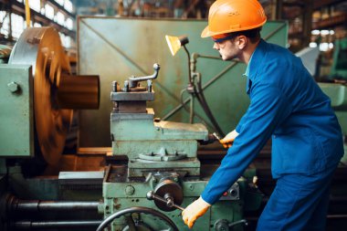 Üniformalı ve kasklı işçiler torna tezgahında çalışıyor, fabrikada. Endüstriyel üretim, metal mühendisliği, güç makineleri üretimi