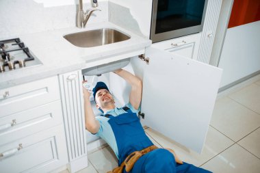 Üniformalı erkek tesisatçı mutfağa boru döşüyormuş. Alet çantası tamir lavabosu ve evde hijyenik ekipman servisi olan bir kadın.