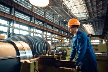 Üniformalı ve kask kontrollü erkek işçi tornayı çalıştırıyor. Endüstriyel üretim, metal mühendisliği, güç makineleri üretimi